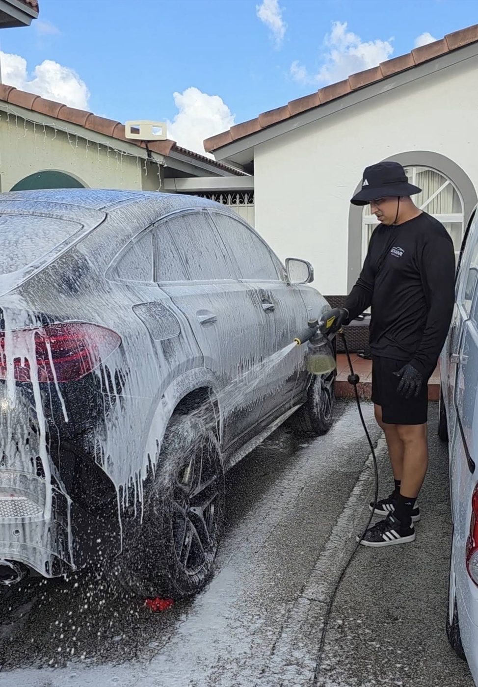 Eduar hand washing a black SUV covered in foam in a Hialeah driveway